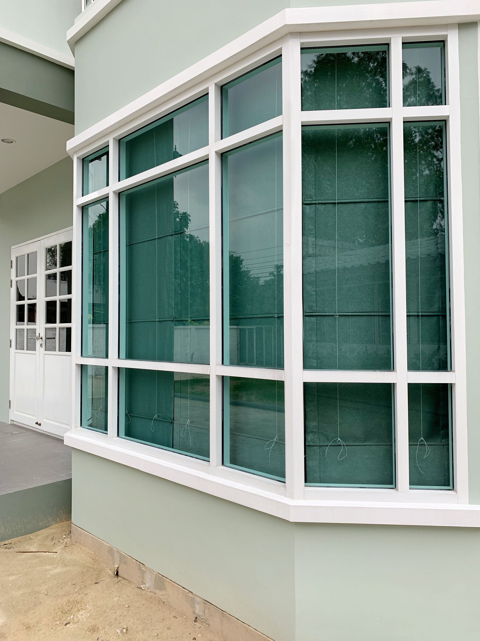 White-trimmed bay windows with green-tinted glass on a cream building exterior