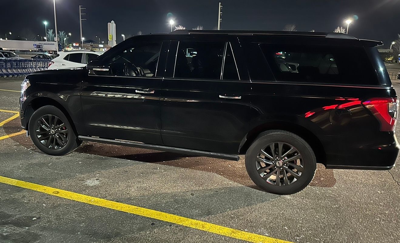 Black SUV parked in a lot at night, viewed from the side under bright lights.