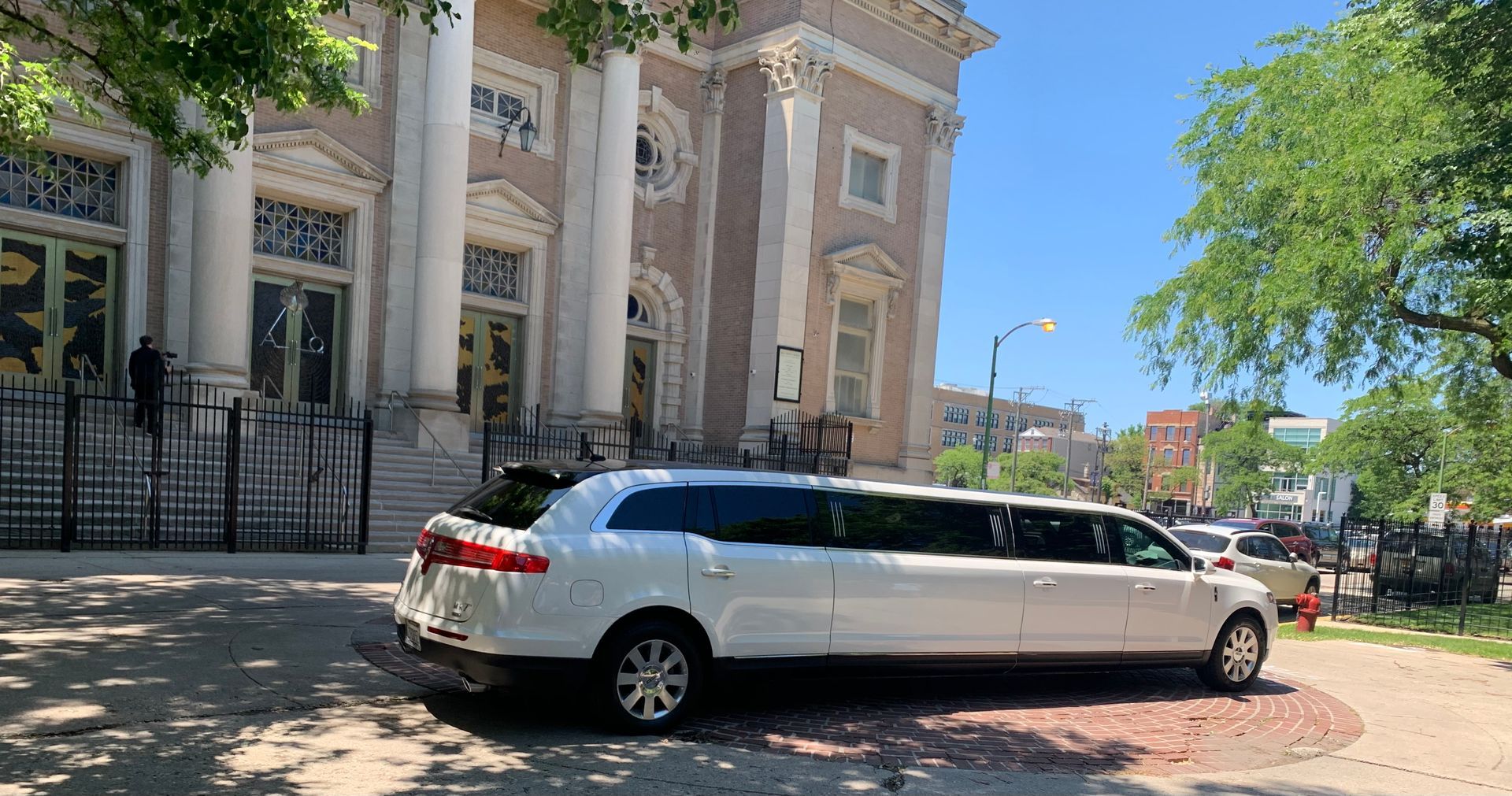 White stretch limousine parked by a historic building on a sunny street