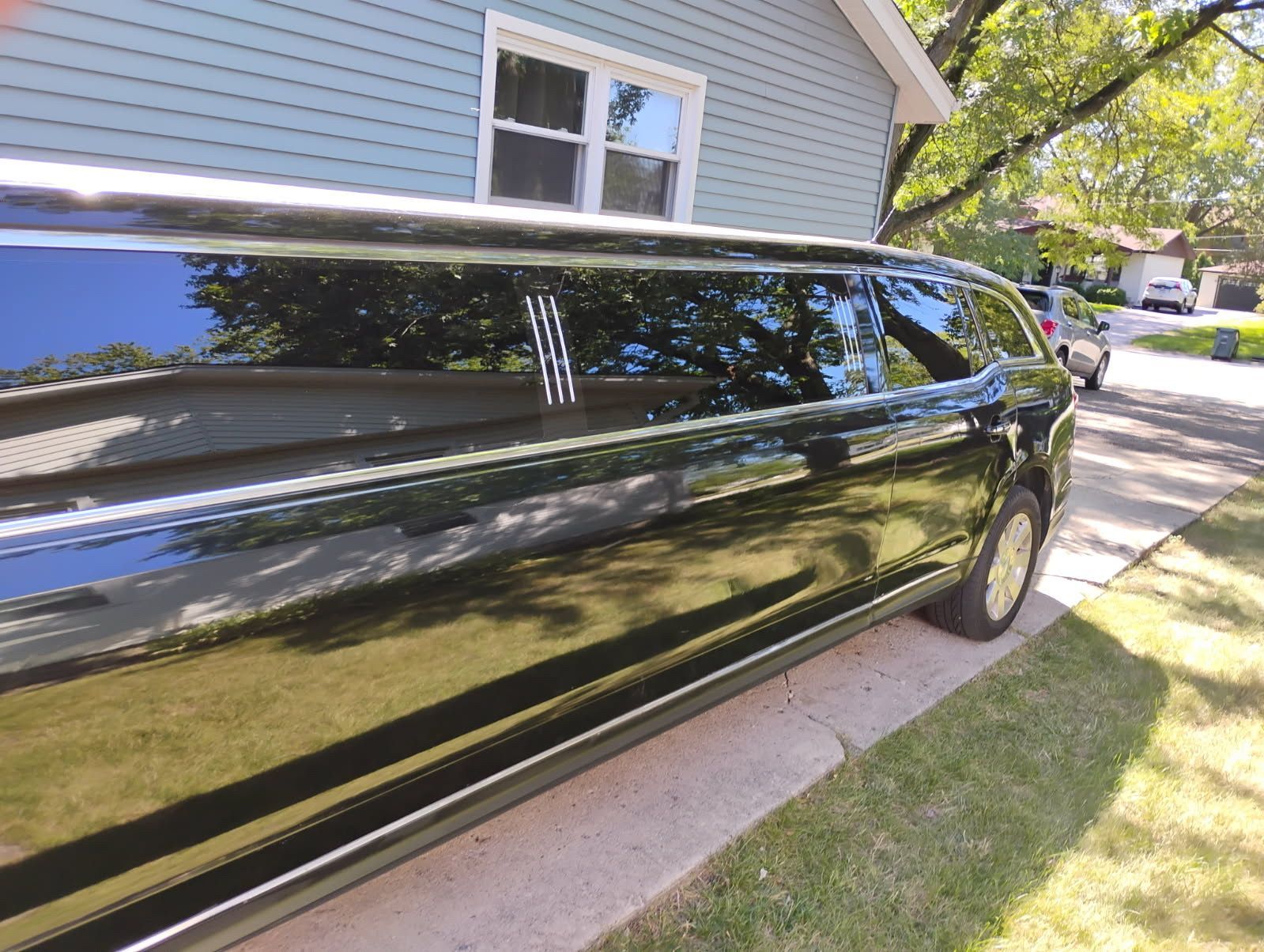 Black limousine parked in a driveway beside a house, viewed from the side.