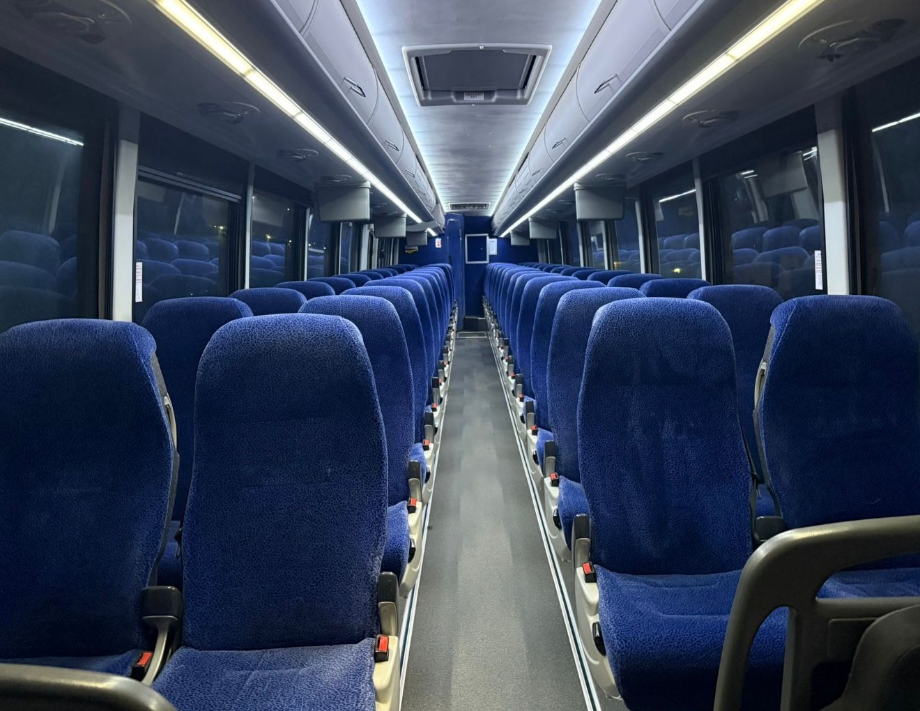 Empty train carriage with rows of blue seats and overhead lights, viewed from the aisle