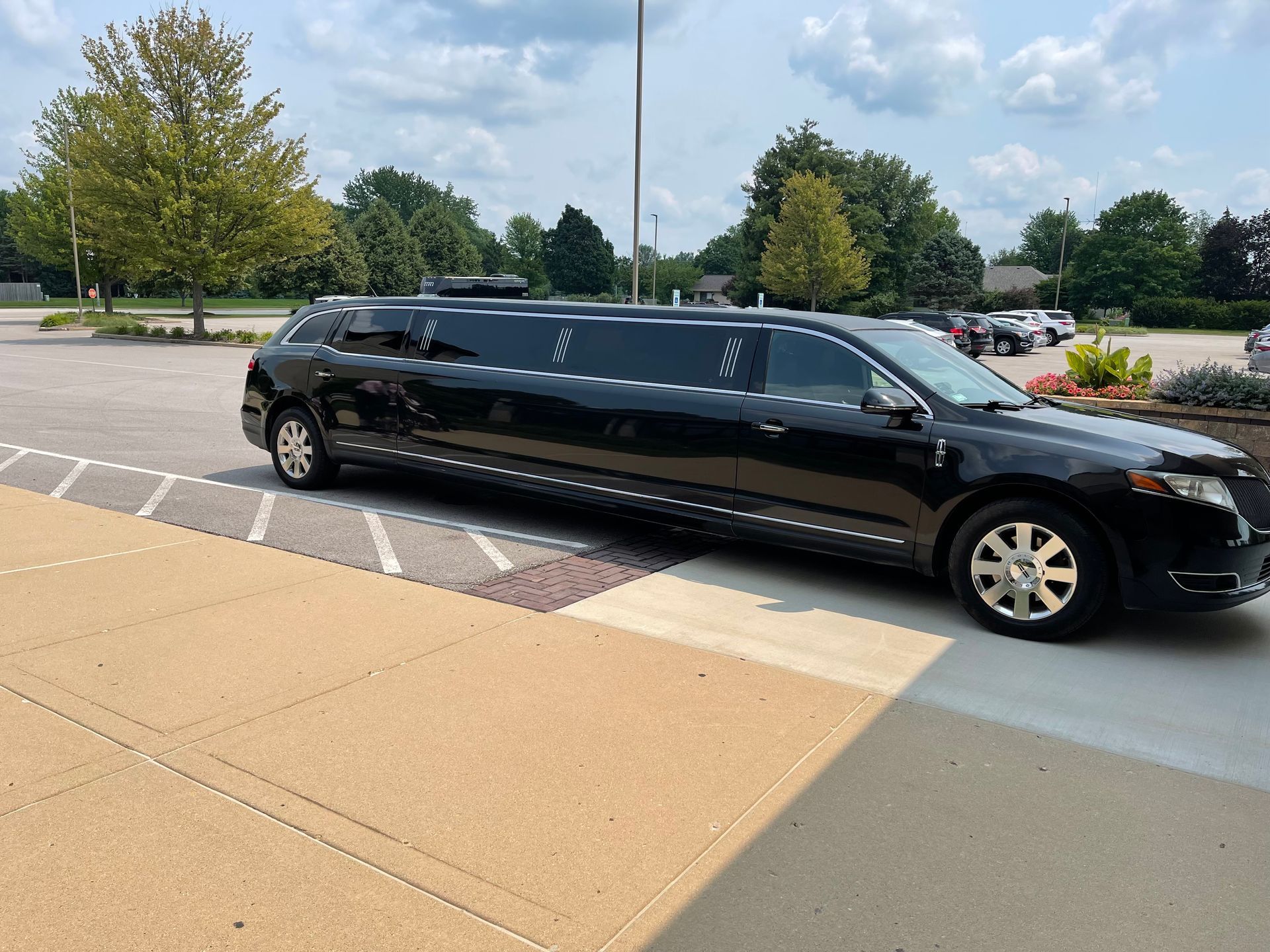 Black stretch limousine parked outside on a sidewalk beside a road and trees