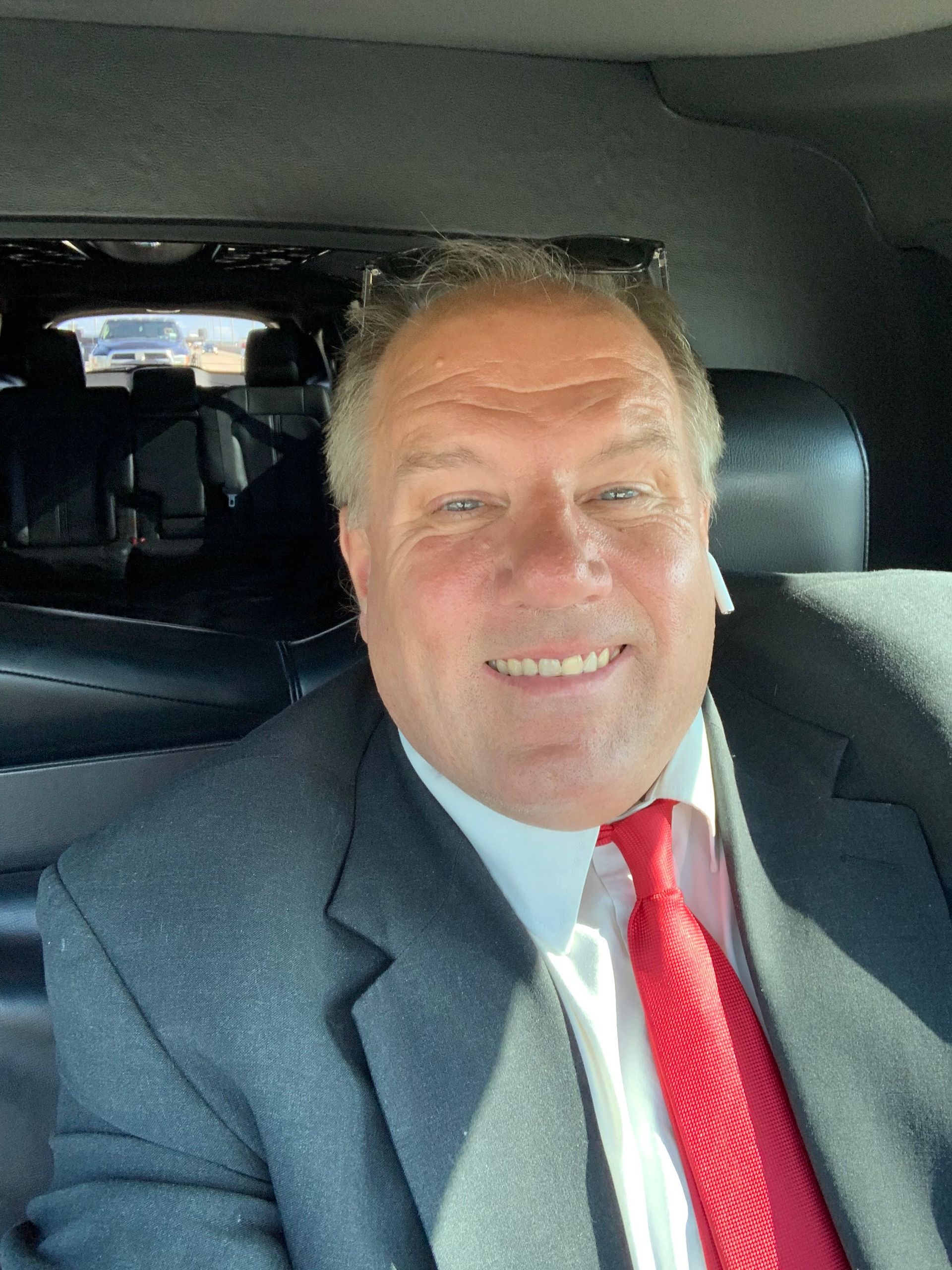 Smiling man in a suit and red tie sitting in a car interior