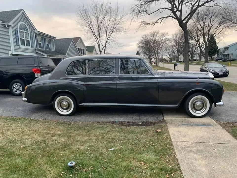 Classic black vintage sedan parked on a suburban street beside a sidewalk and lawn.