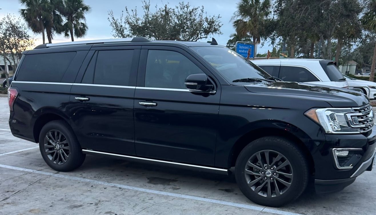 Black SUV parked in a lot, side view with palm trees in the background
