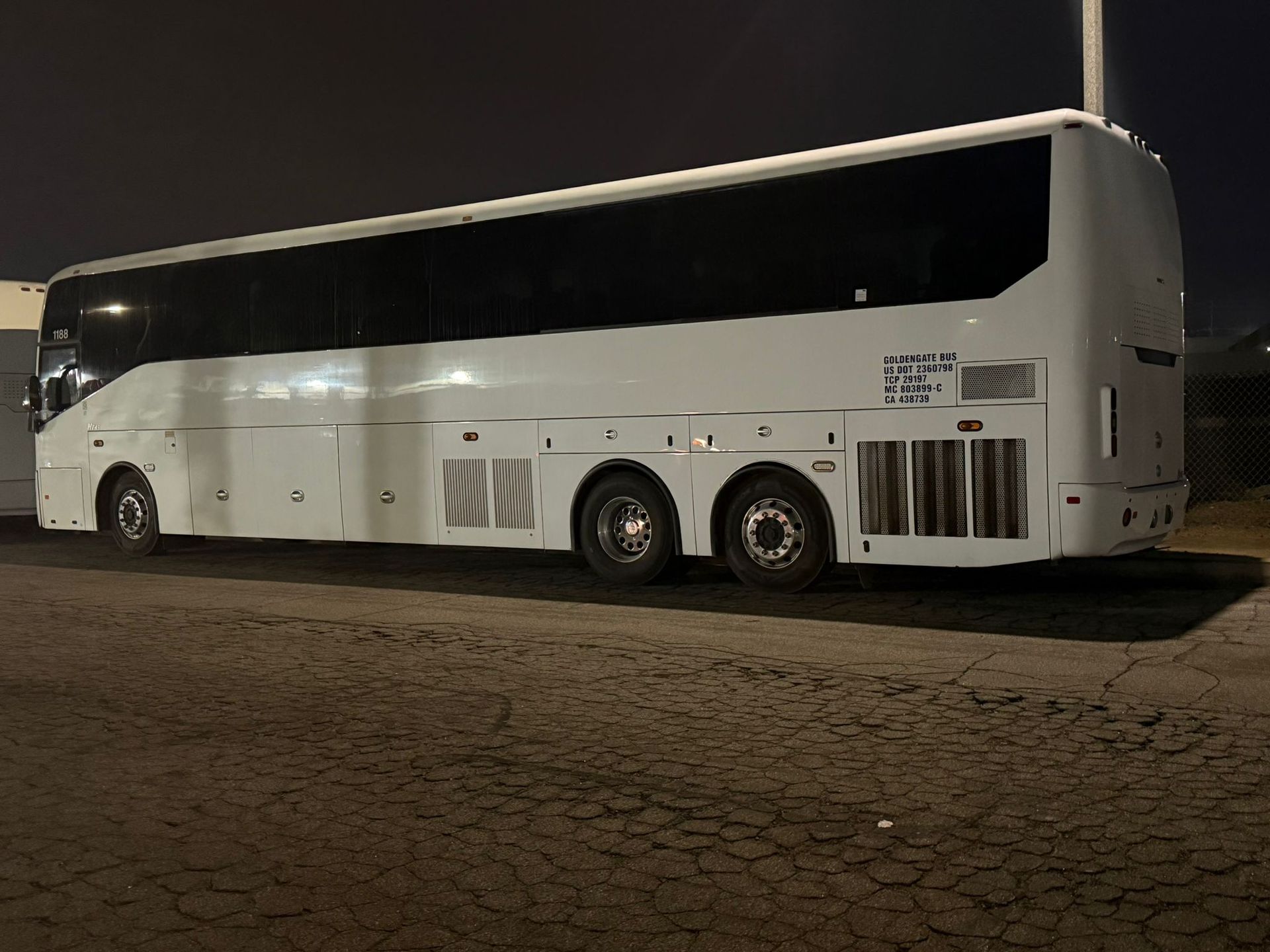 White and black double-decker tour bus parked on a dimly lit street at night