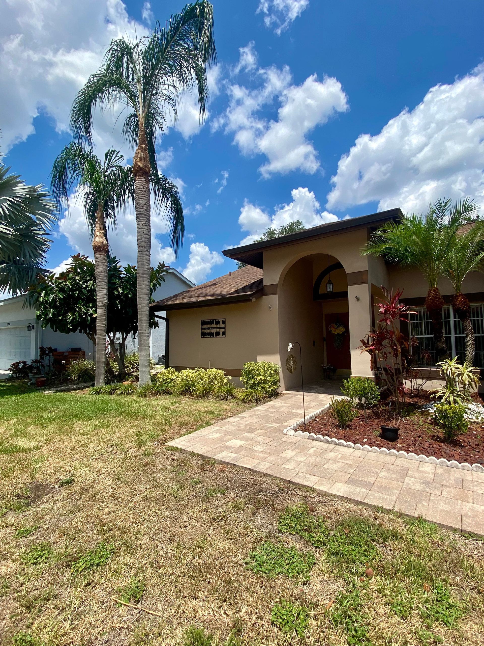 A house with a lot of grass and palm trees in front of it.