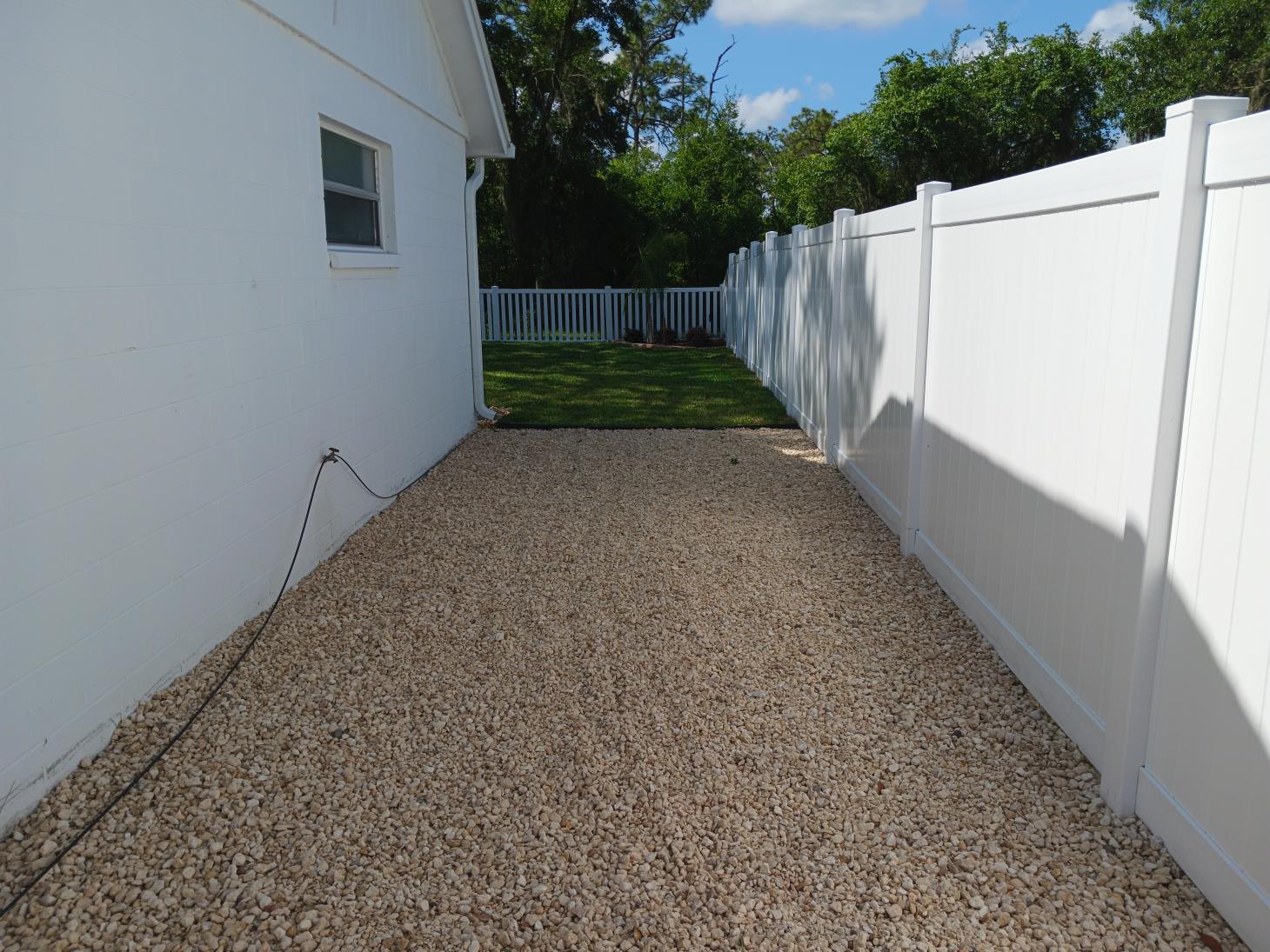A white fence surrounds a gravel driveway in front of a house