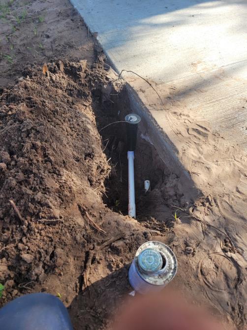 A person is digging a hole in the ground to install a sprinkler.