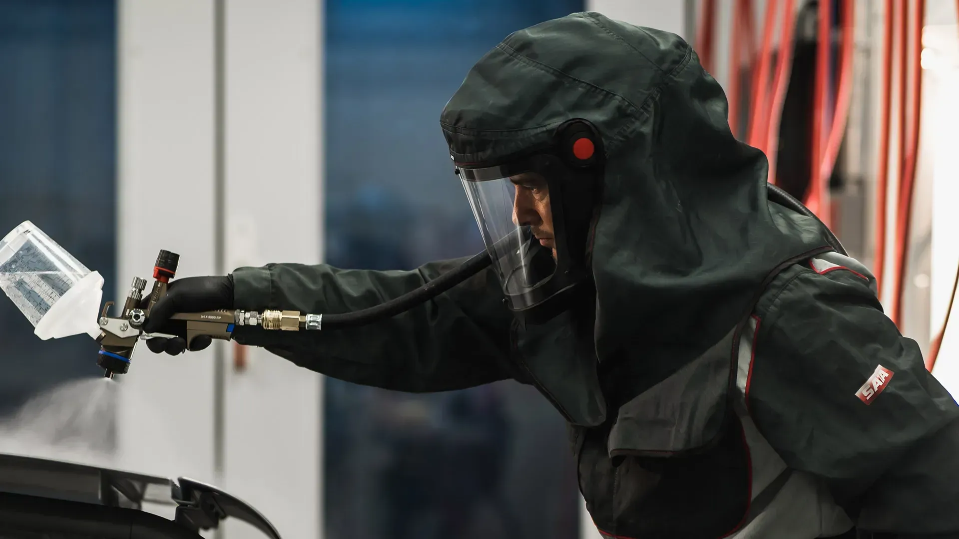 Un homme portant une veste à capuche et un casque peint une voiture à la bombe.