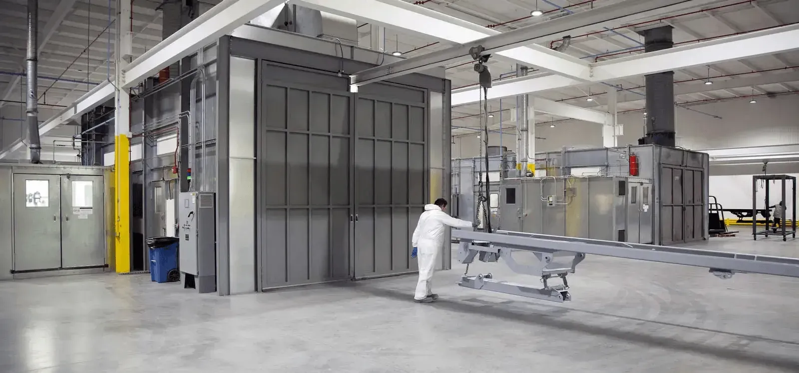 A man is standing in a factory holding a piece of metal.