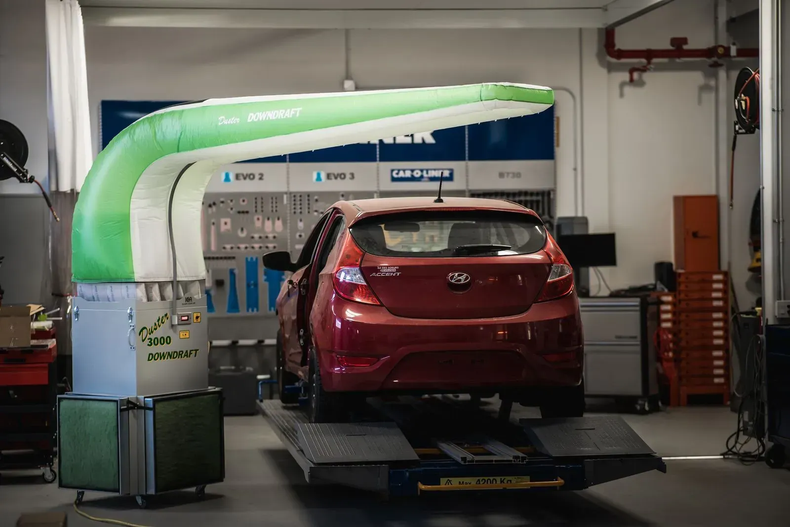 A red car is sitting on a lift in a garage.