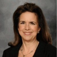 Woman with brown hair, wearing a black blazer and necklace, smiling at the camera.