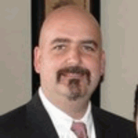 Bald man in a suit smiles at the camera, with a goatee and a pink tie.