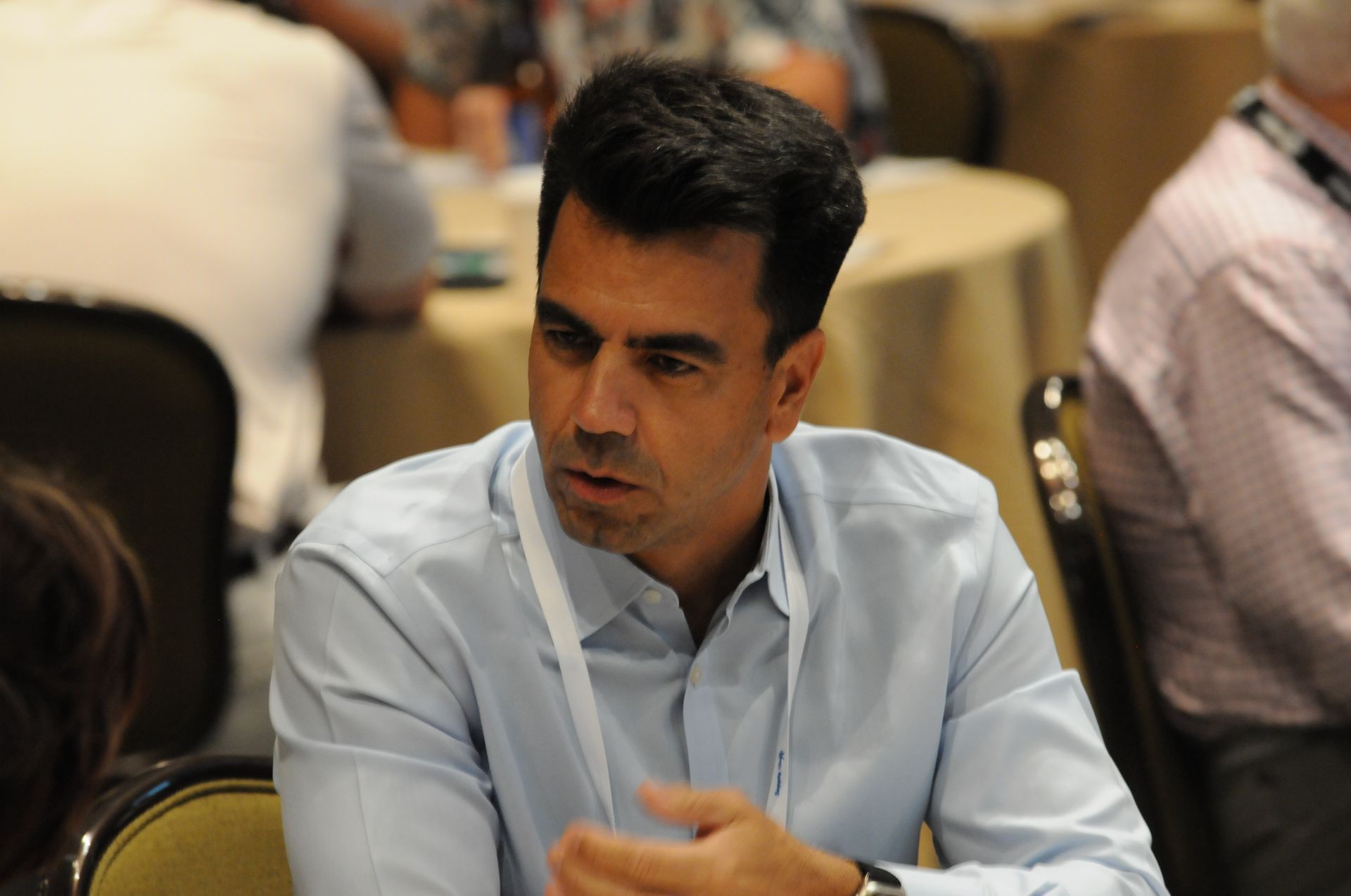Man in a blue shirt at a conference, looking to his right and speaking.