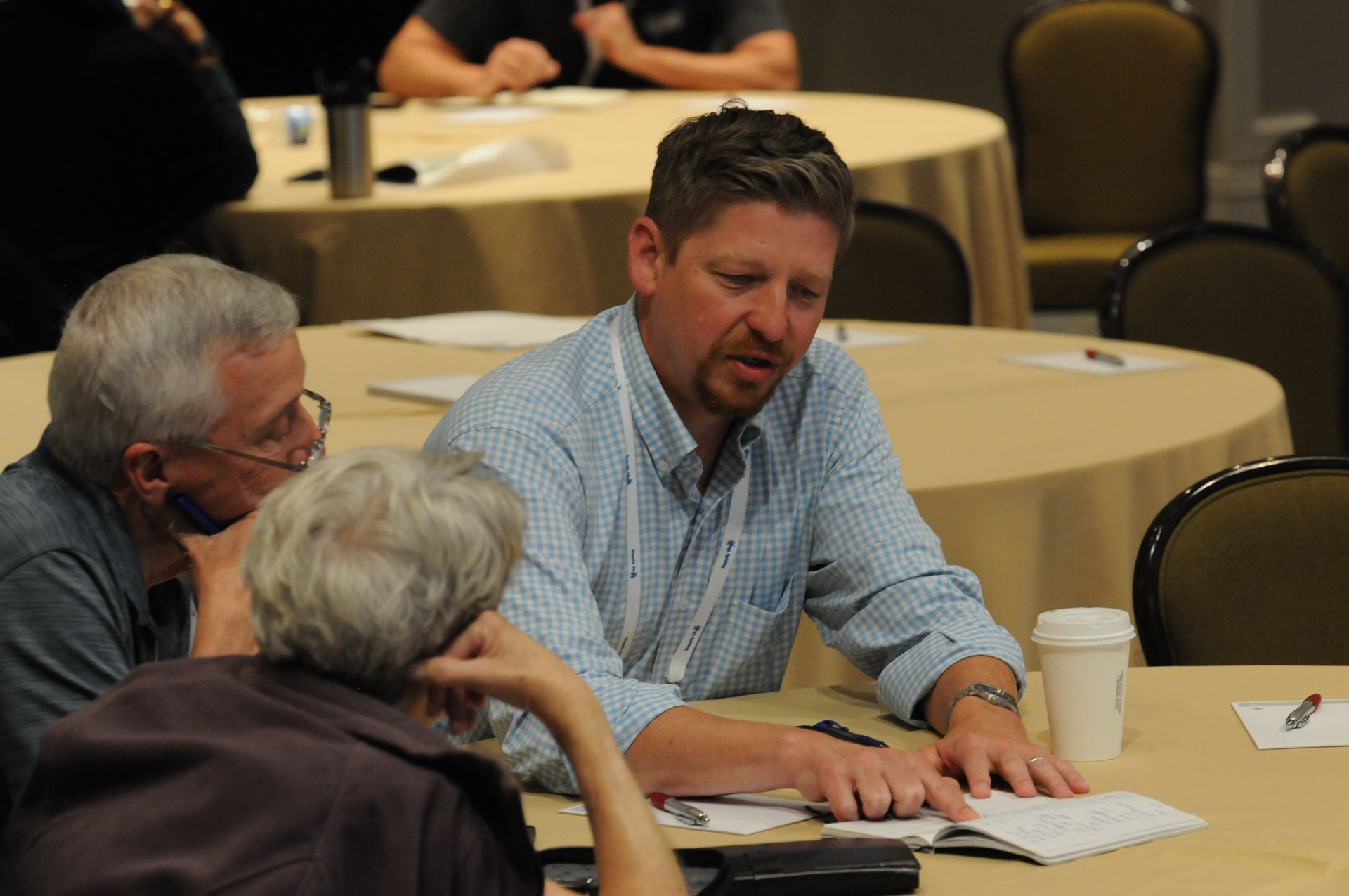Three people seated at a table, discussing papers, in a conference setting.