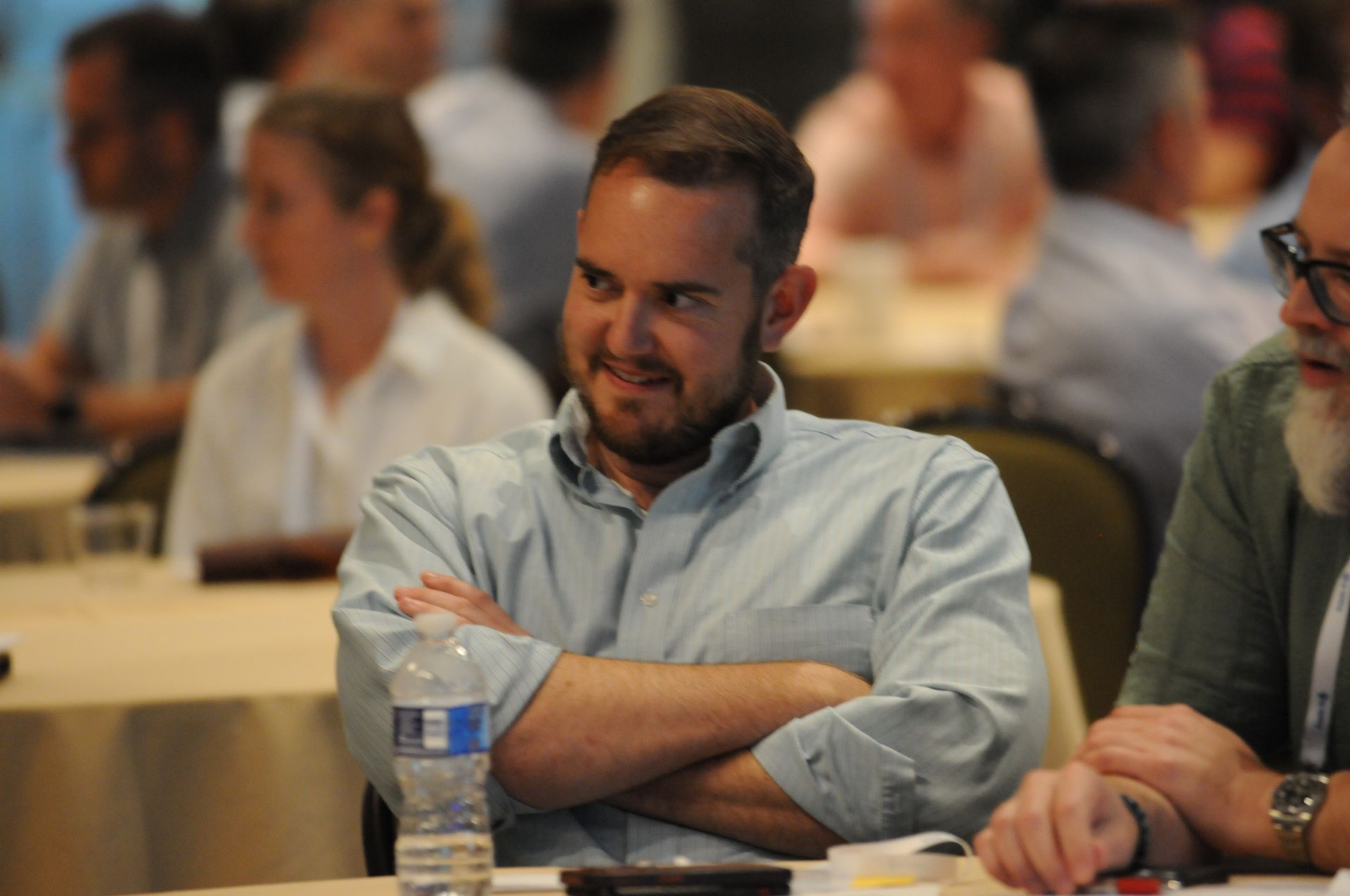 Man with crossed arms and a slight smile at a conference table.