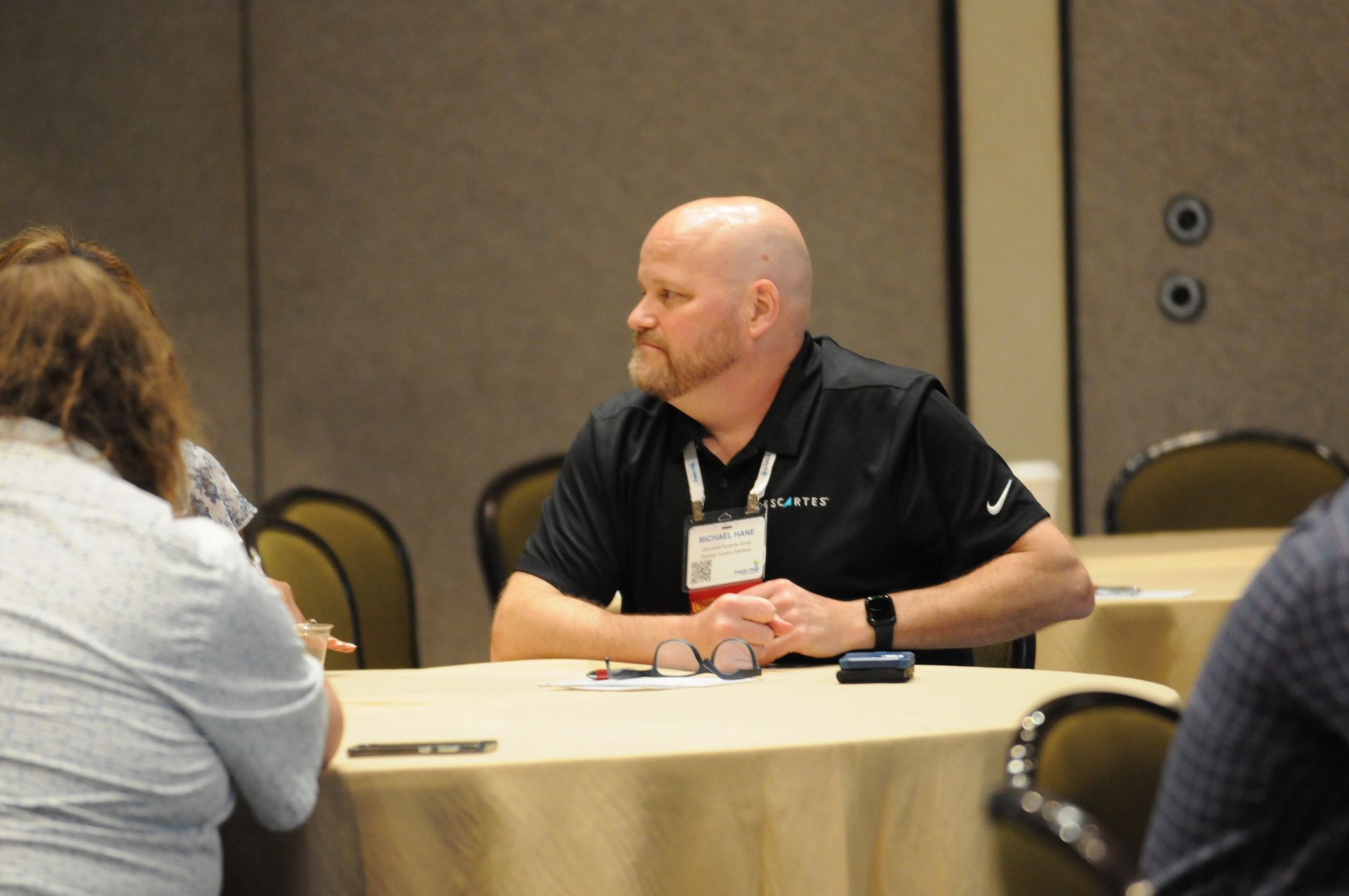 Man at a round table in a meeting, wearing a black shirt and looking to the side.