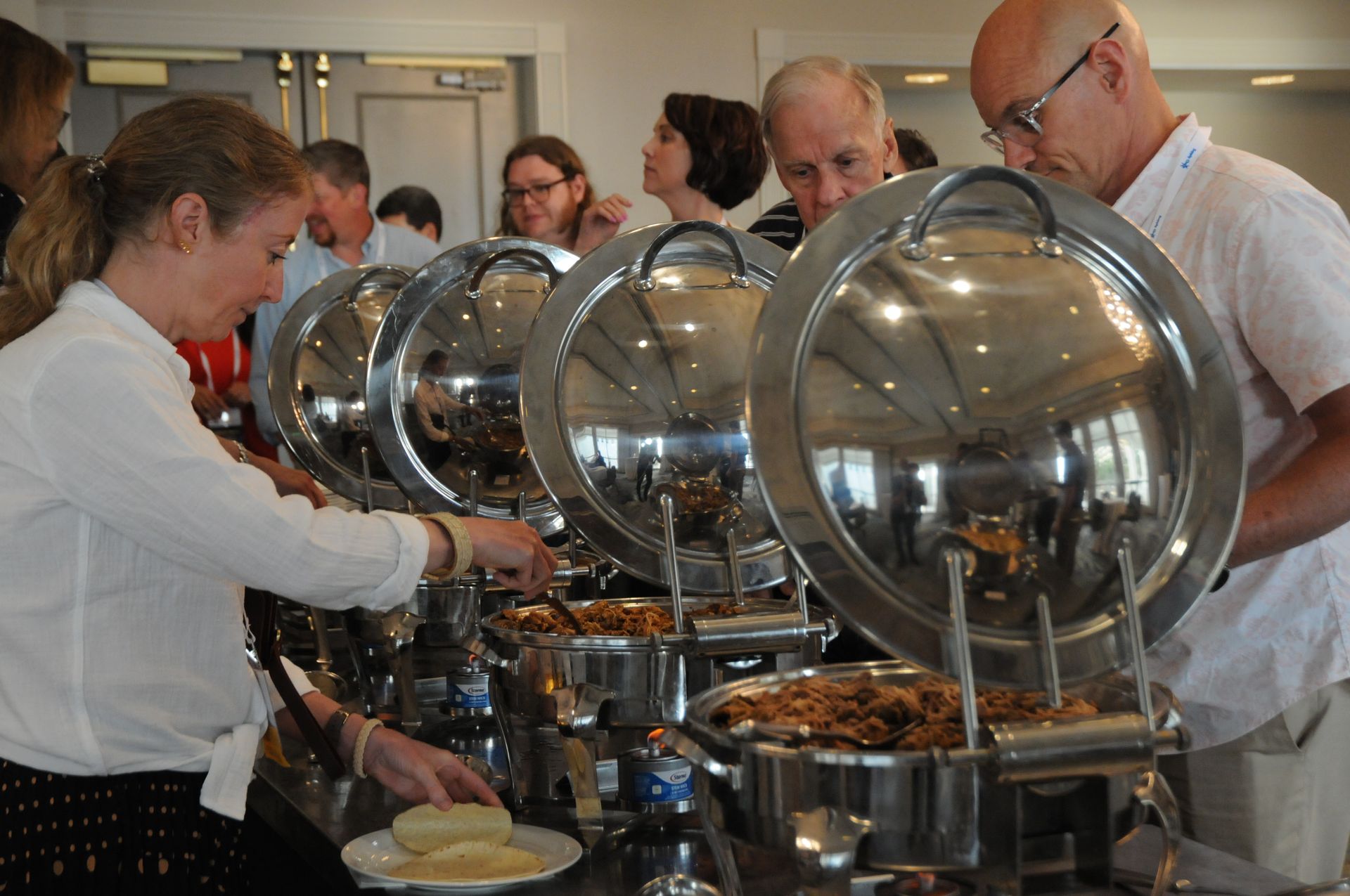People at a buffet, choosing food from covered serving dishes.