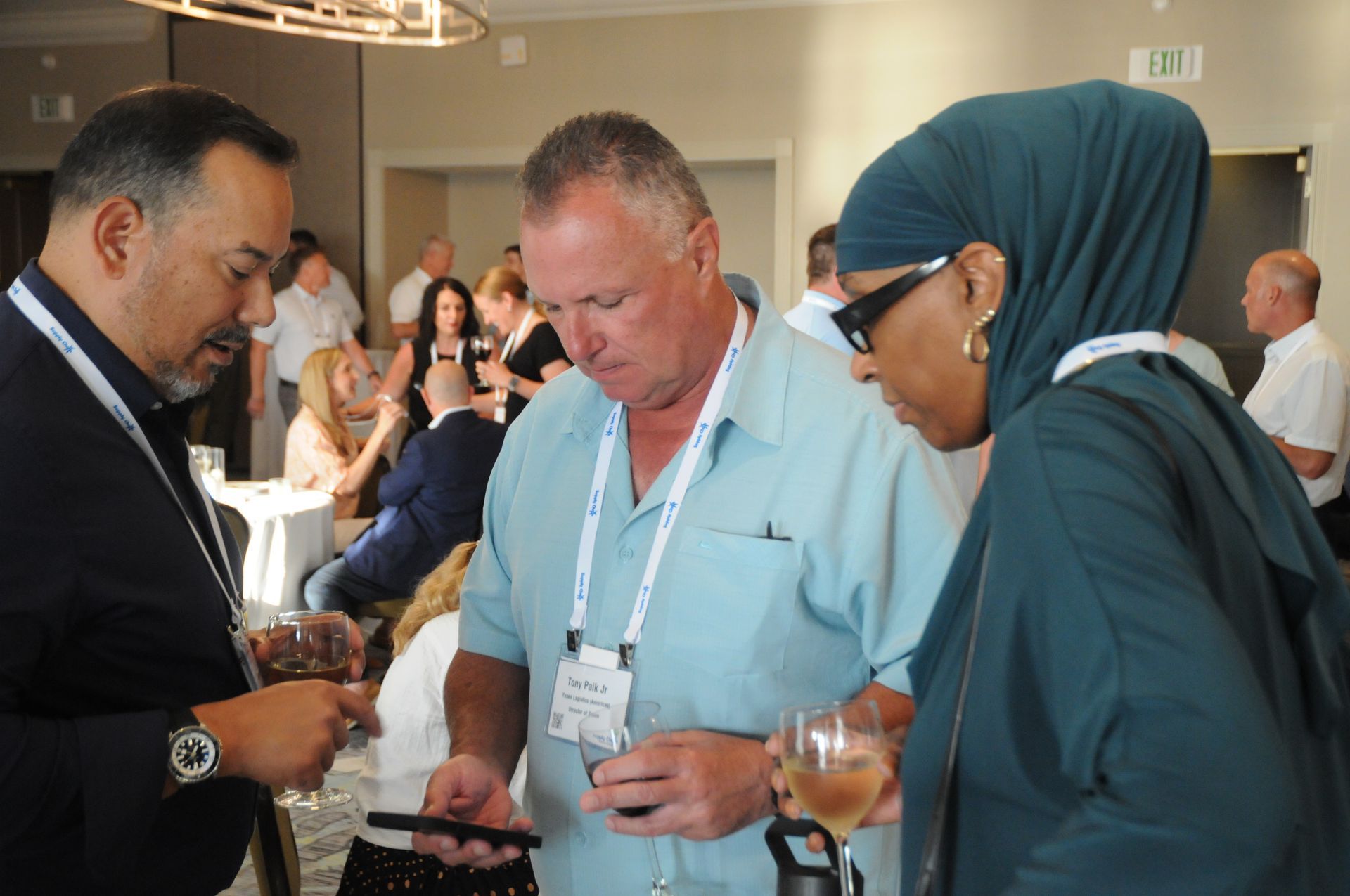 Three people look at a phone together at an event. One wears a hijab, another a light blue shirt.