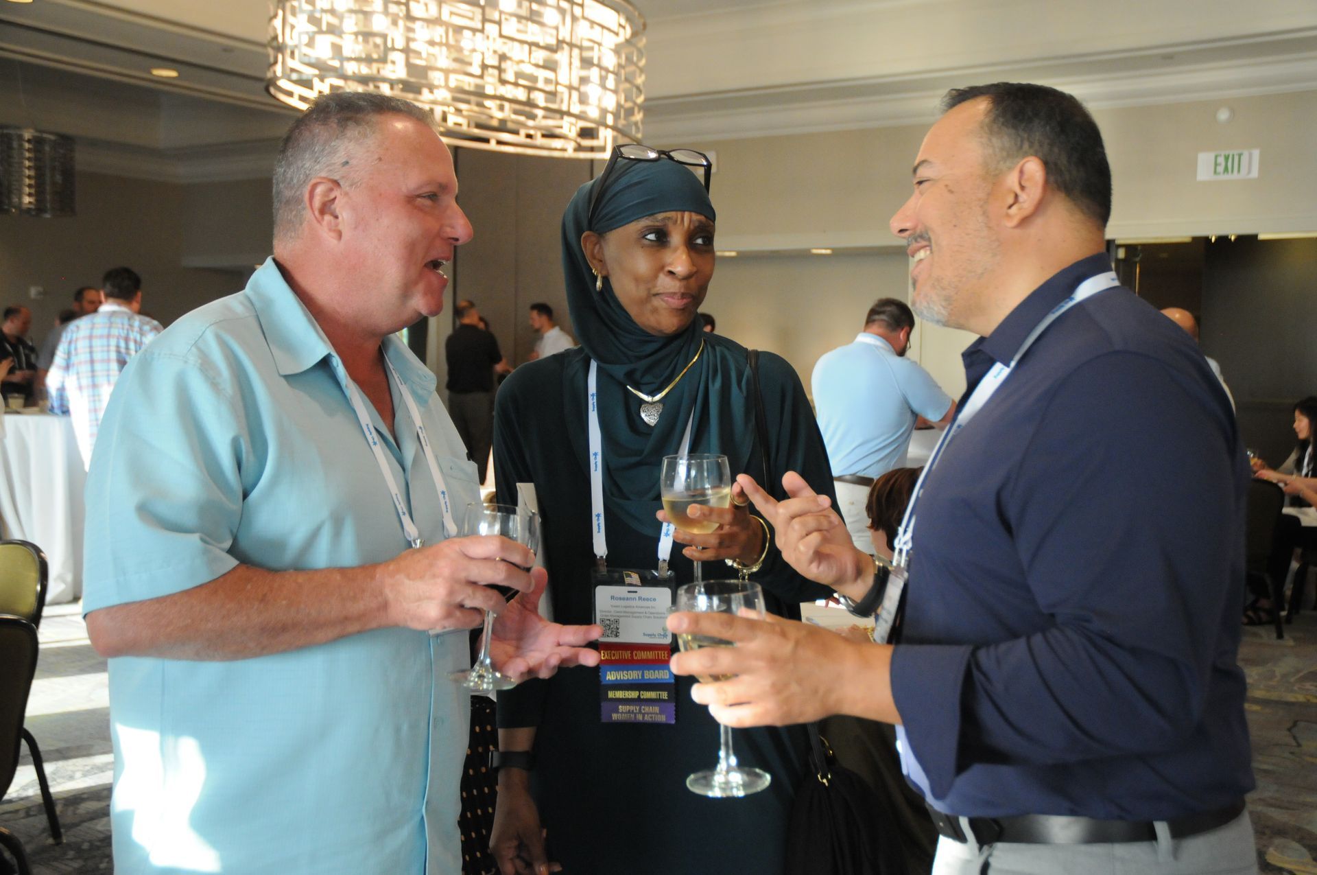 Three people, two men and a woman, conversing at an event. They are holding glasses and smiling.