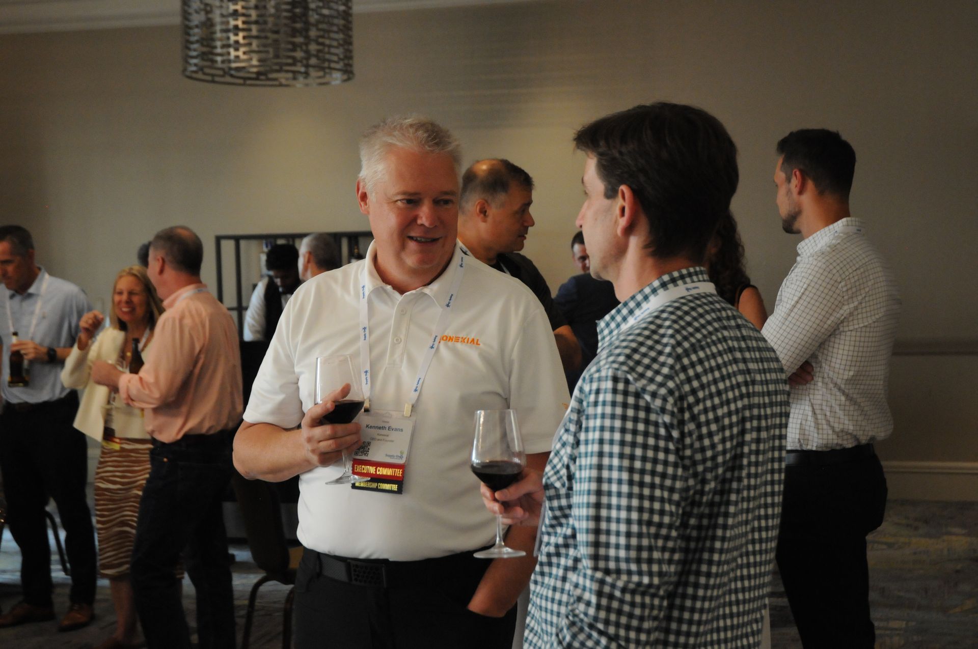 People at a business event, conversing and holding drinks. Interior, neutral tones.