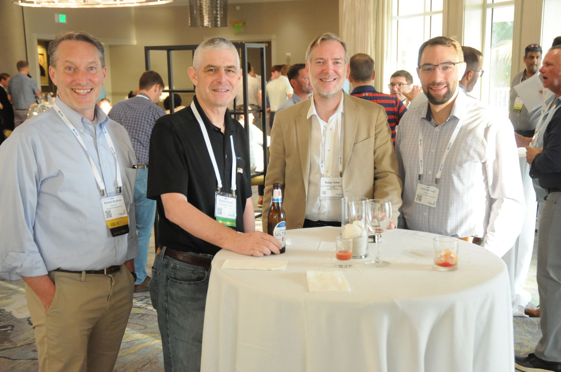 Four men at a networking event around a small table. They smile, wearing name tags, in a well-lit room.