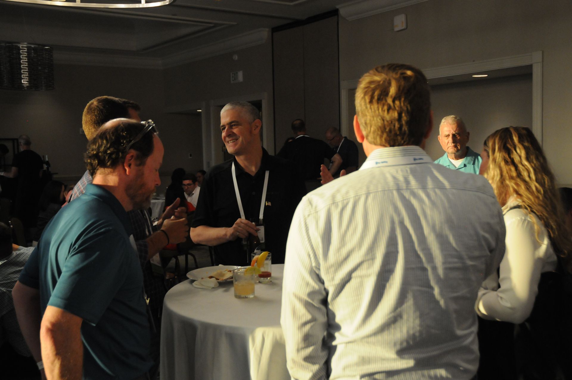 People at a conference networking. Several people stand around a small table, chatting.