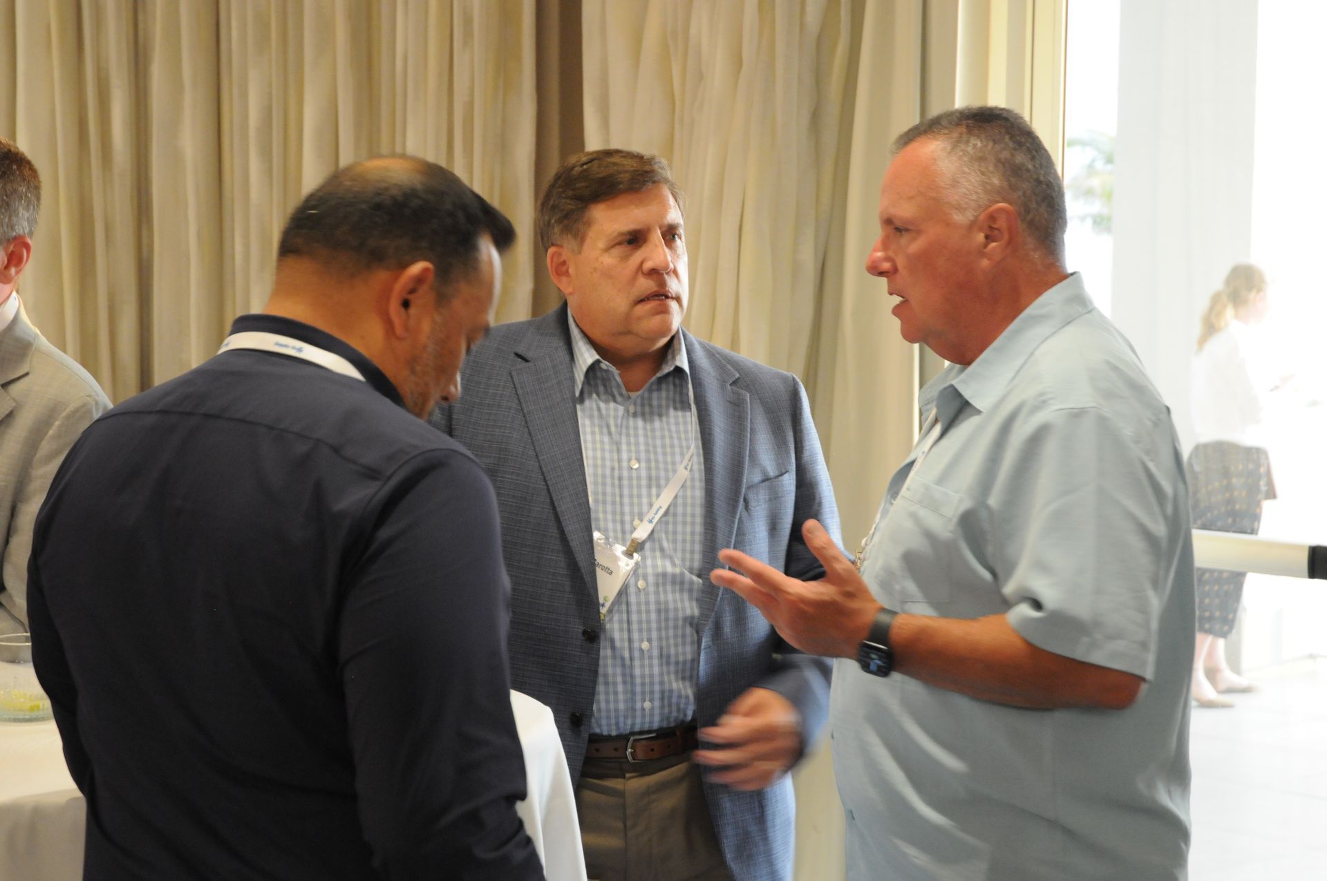 Three men in suits conversing at an event, possibly a conference.