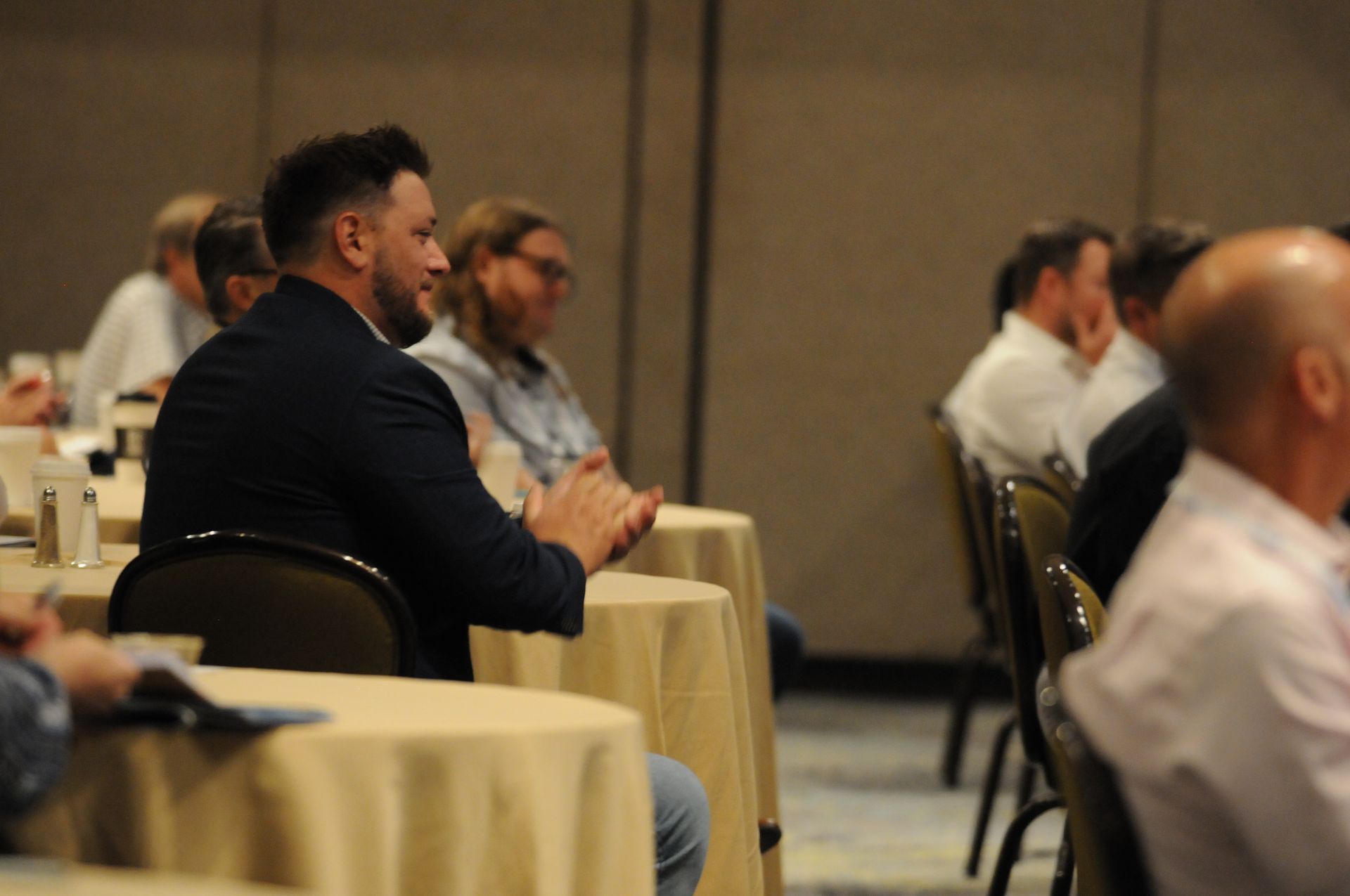 People in an audience at tables clap during a conference.