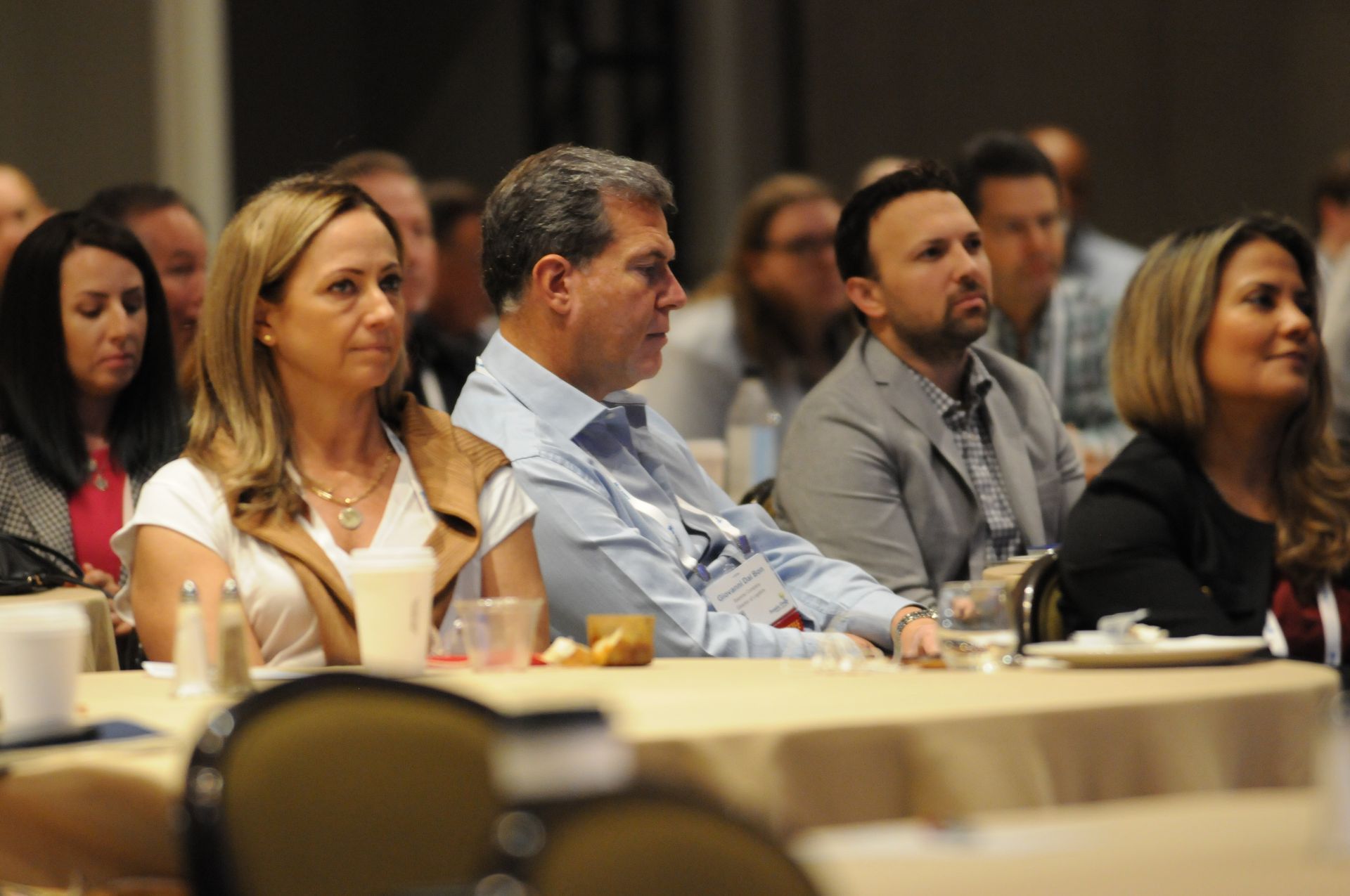 People seated at tables in a conference room, listening attentively.