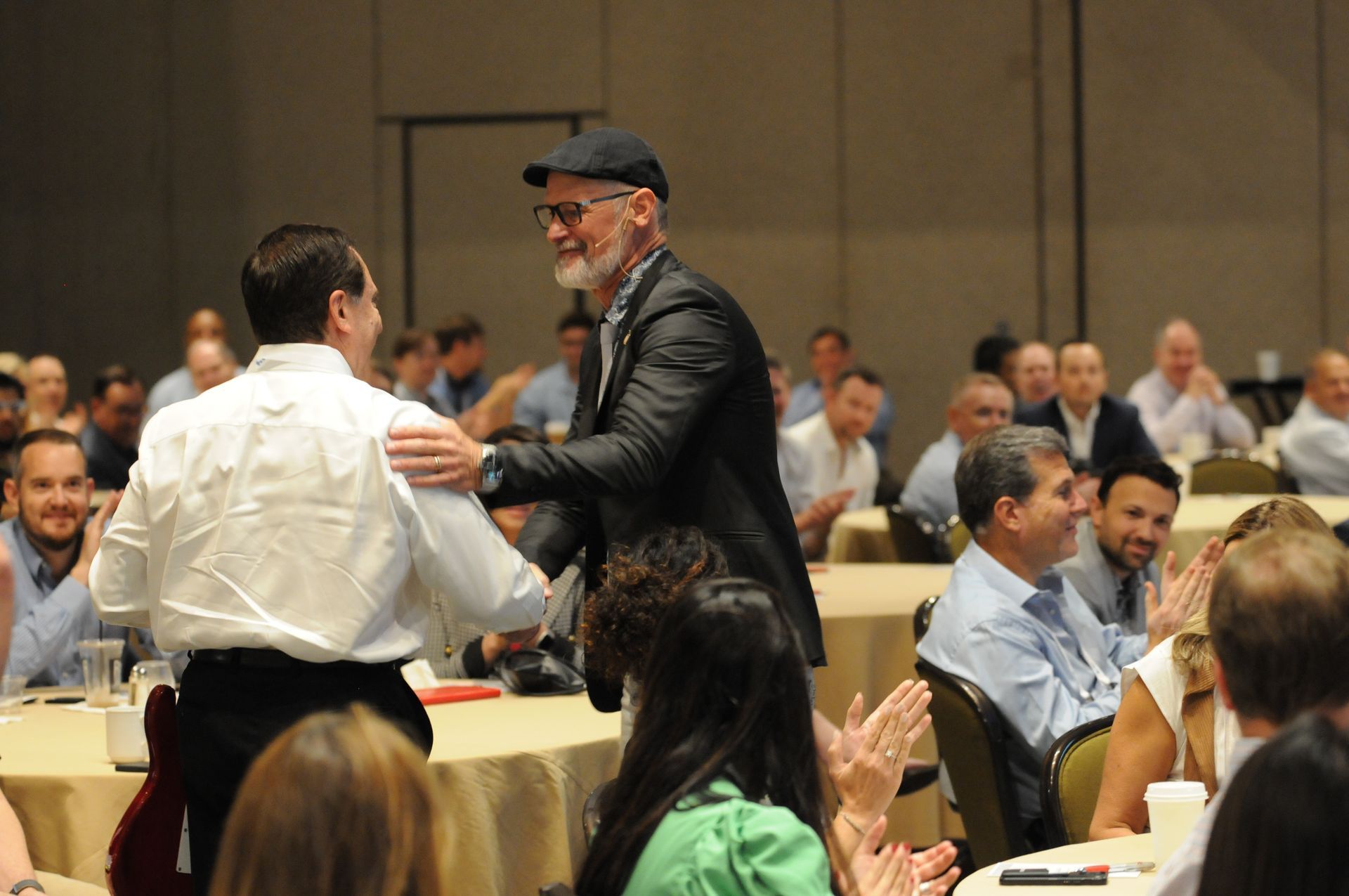 Two men shaking hands at an event. Applause from the audience in a large room.