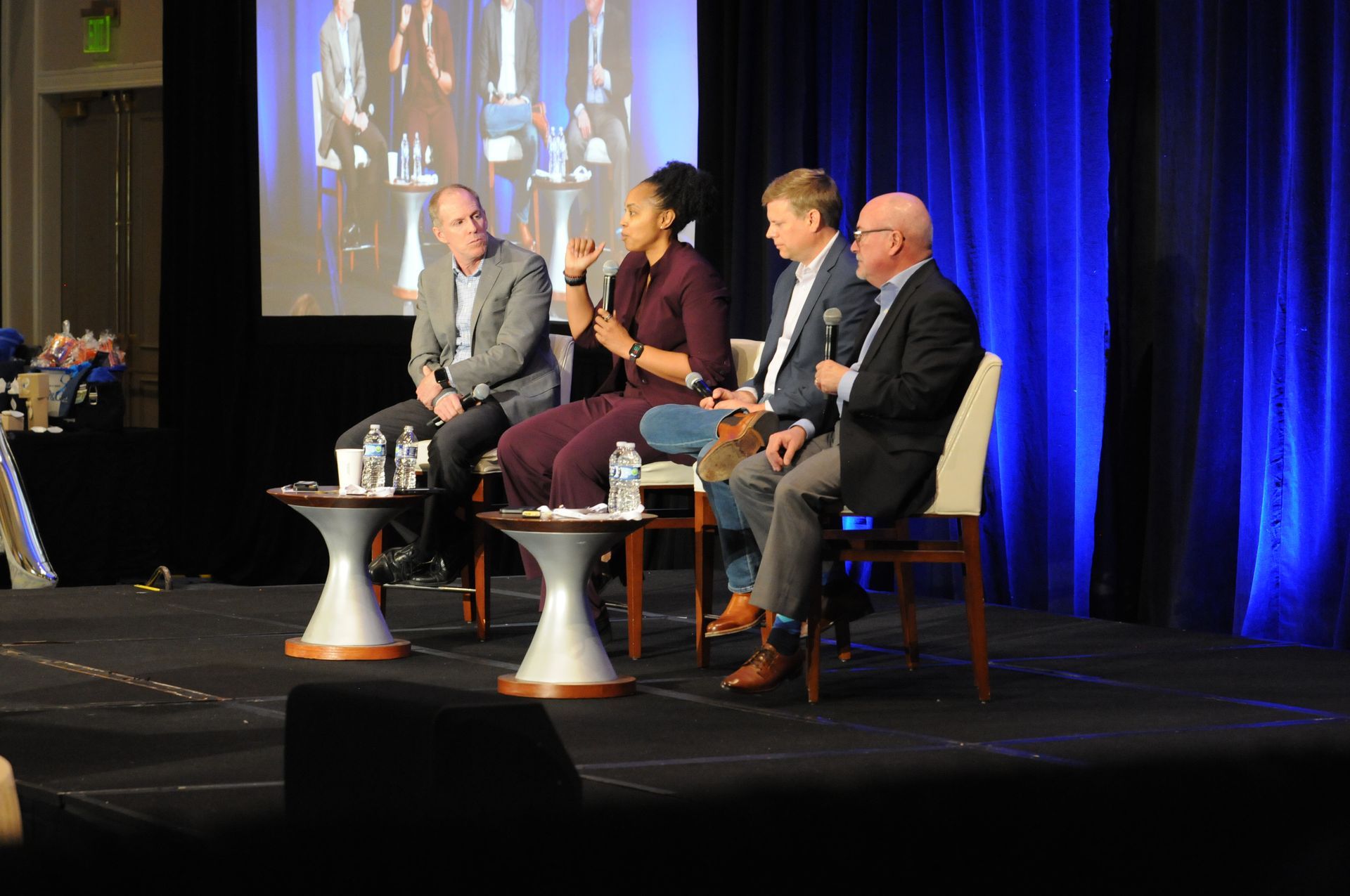 Panel of four people on stage with a screen behind them. They are discussing.