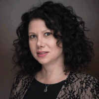 Woman with curly dark hair, wearing a black top and lace-patterned jacket, smiling.