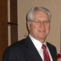 Man in suit, wearing glasses, smiling.