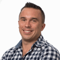 Man with short brown hair smiling, wearing a blue and white checkered shirt.