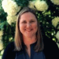 Woman with blonde hair smiles in front of white flowers.