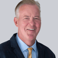 Smiling, middle-aged man in a navy suit and gold tie, looking at the camera.