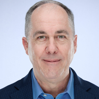 Man with short gray hair, wearing a blue shirt and navy blazer, smiles.