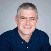 Man with short gray hair and blue shirt smiling.