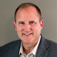 Man in a suit smiles, looking at the camera.
