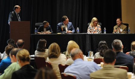 Panel of five people at a conference table addressing an audience.