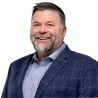 Smiling man with gray beard, wearing a blue suit jacket and button-down shirt.