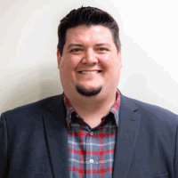 Smiling man in a blue blazer over a red and gray plaid shirt, set against a white background.