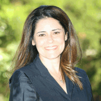 Woman with dark hair and a smile, wearing a dark blue suit.