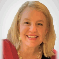 Blonde woman smiling, wearing red scarf, gold earrings and necklace.