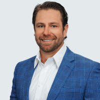 Man with short brown hair, wearing a blue plaid blazer and white shirt, smiling at the camera.