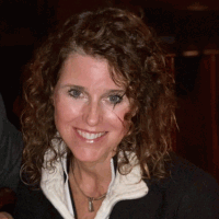Woman with curly brown hair smiles at camera, wearing a black jacket and white collar.