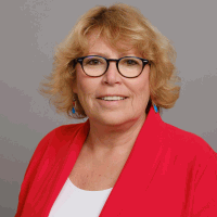 Woman with glasses, blonde hair, wearing red blazer and white shirt; smiling.