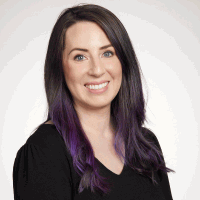 Woman with dark hair and purple highlights smiles at the camera, wearing a black shirt.